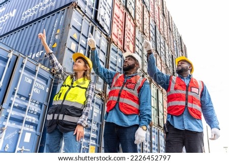 Photo of a team of engineers of male and female pointing to sky together looking front with determination and hope in front a stacks full of containers in a container shipping dock yard Royalty-Free Stock Photo #2226452797