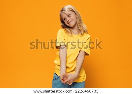 a cute, shy, beautiful school-age girl in yellow clothes stands against a bright, yellow background. Horizontal photo with empty space for inserting advertising text