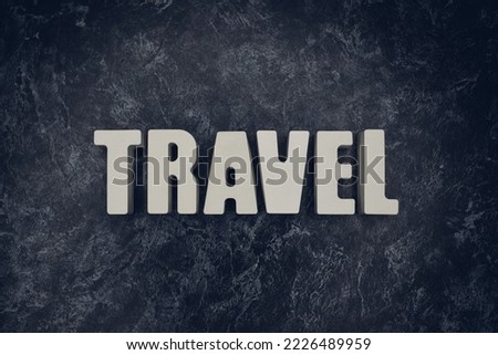 The inscription "Travel" in white letters on a black marble background.
