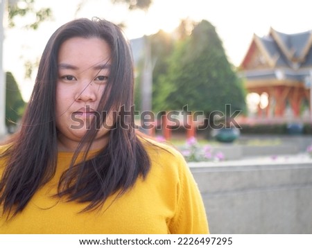 Portrait of an Asian woman, chubby, beautiful cute long black hair wearing black long sleeves, smiling. happily inside the park With happiness and peace of mind, relax during the evening time at sun