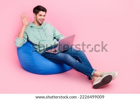 Full length photo of positive boy sit chair trendy clothes use netbook communicate colleagues empty space isolated on pink color background