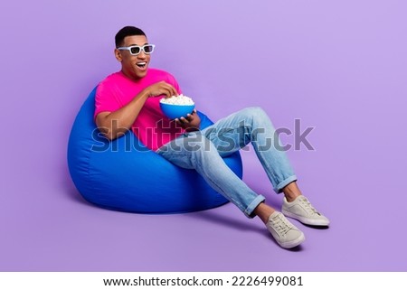 Full body photo of crazy astonished person sit cozy bag hold popcorn plate isolated on violet color background