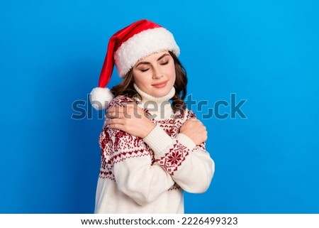 Photo of dreamy adorable lady wear print pullover santa headwear closed eyes embracing herself isolated blue color background