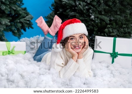 Photo of dreamy sweet girl dressed santa claus helper hat lying x-mas snow under firs isolated blue color background