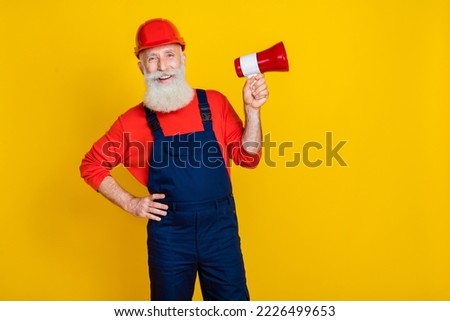 Photo of happy smiling age man wear overall uniform red hard hat holding bullhorn empty space isolated yellow color background