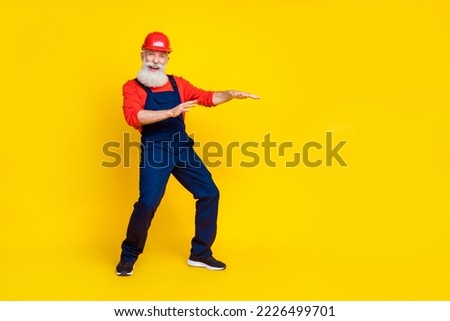 Photo of cool funny senior guy dressed uniform overall red hardhat having fun empty space isolated yellow color background