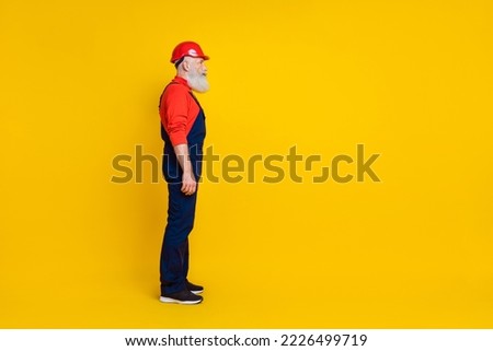 Photo of serious confident age man workwear overall red hard hat looking empty space isolated yellow color background