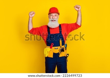 Photo of positive strong old guy dressed uniform overall red hardhat rising hands showing biceps isolated yellow color background