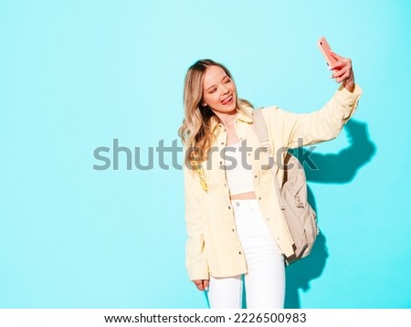 Young beautiful woman looking at camera.Trendy female smiling in casual summer clothes. Positive and funny model posing on grey background in studio with backpack. Taking selfie