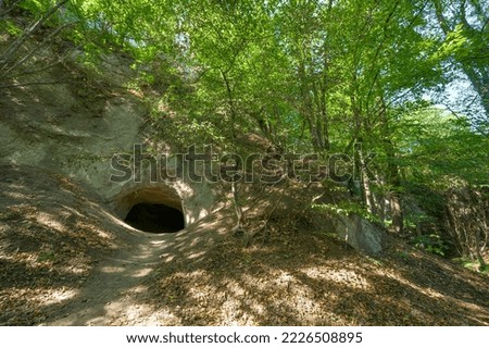 Dark and mysterious cave entrance in the Brohltal in Rhineland-Palatinate, Germany. A volcanic formation in the Eifel region with natural caves and lush green forest.  Royalty-Free Stock Photo #2226508895