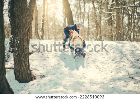 Children sled down the hill in the winter park. Children in the winter snowy forest on a sled. It is snowing, children are playing on the hill.