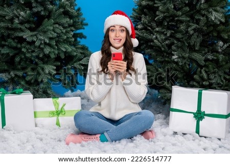 Full body portrait of excited funny girl sit snow use telephone bite lips pine fir tree isolated on blue color background
