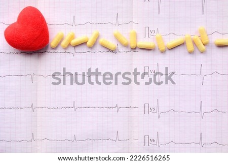 Red heart and yellow pills on sheet of pink millimeter paper with diagram of medical examination of the heart on an electrocardiogram with copy space. Medical concept Royalty-Free Stock Photo #2226516265