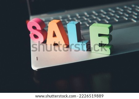 Funny word Sale set on notebook bottom. Colorful sign Sale on black surface at black screen background. Shopping online concept. Internet marketing. E-commerce. Wooden letters promote e-shopping.