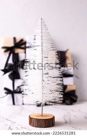 Modern white decorative Christmas tree in front of group of wrapped boxes with presents on white textured backgrond. Place for text.