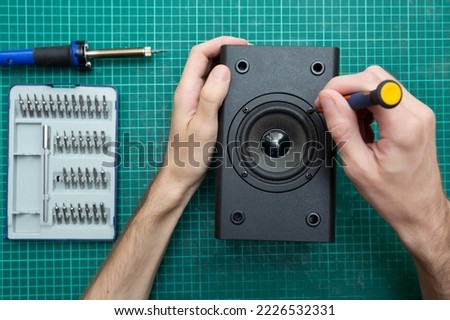 Master holds a screwdriver while repairing an audio speaker. Workplace with a screwdriver and soldering iron. Top view. Flat lay.