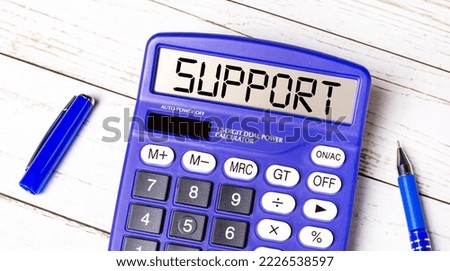 Flat lay or top view of blue pen and calculator with SUPPORT text on light wooden table.