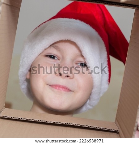 Little Christmas girl in a Santa hat looks into a gift box. Child is happy with a New Year's gift. The background is defocused light. The concept of Christmas and New Year 2022. High quality photo