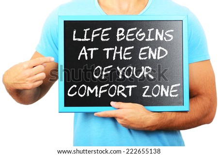 Man holding blackboard in hands and pointing the word LIFE BEGINS AT THE END OF YOUR COMFORT ZONE