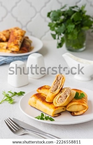 Thin pancakes stuffed with boiled minced meat with fried onions on a white plate on a light concrete background. Pancake recipes. International Pancake Day.