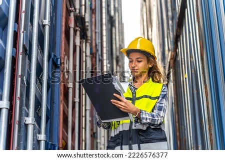 Photo of a young beautiful professional western female brunette engineer supervisor inspecting containers in a shipping containers yard to ensure the content and delivery information is correct Royalty-Free Stock Photo #2226576377