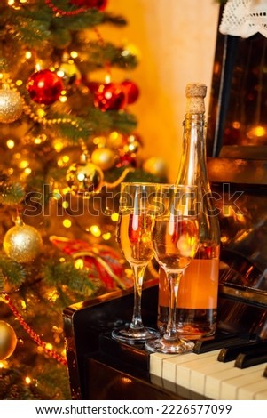 Celebrating Christmas with champagne. Two glasses of champagne or wine and bottle on piano near decorated christmas tree all in bright lights