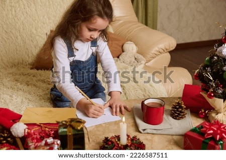 Adorable Caucasian preschool child, a cute little girl draws picture, writes letter to Santa, expecting the upcoming winter holidays. Magical Christmas mood. New Years preparations. December 25