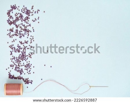 Hobby, craft, needlework or beading concept. Minimalist flat lay, top view. Creative minimalist background with space for text. Purple glass beads, needle and thread for embroidery. 