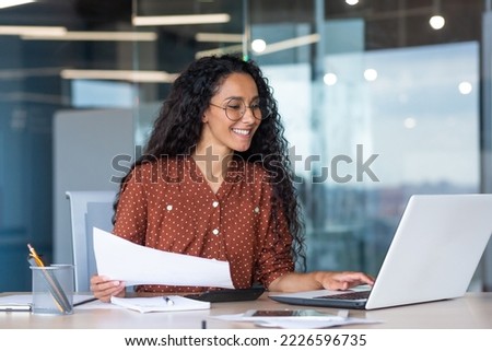 latin american businesswoman working inside office with documents and laptop, worker paperwork calculates financial indicators smiling and happy with success and results of achievement and work Royalty-Free Stock Photo #2226596735