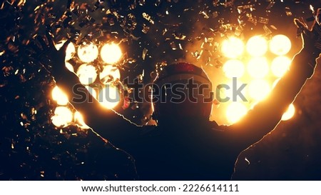 Silhouette of race car driver celebrating the win in a race against bright stadium lights. 100 FPS slow motion shot Royalty-Free Stock Photo #2226614111