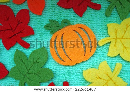 Pumpkin and colorful Maple leaves out of felt on a light green fabric as a background