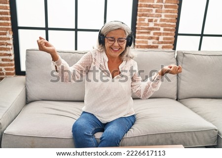 Middle age woman listening to music sitting on sofa at home