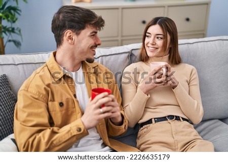 Mand and woman couple drinking coffee sitting on sofa at home