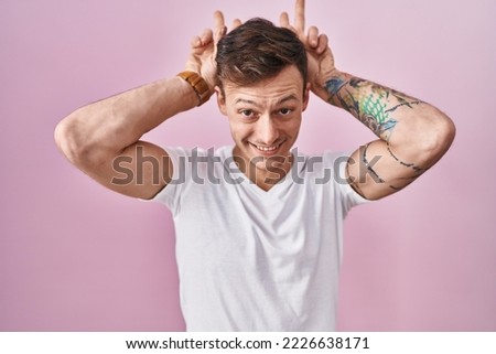 Caucasian man standing over pink background posing funny and crazy with fingers on head as bunny ears, smiling cheerful 