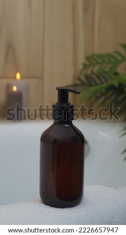 Black bottle of bubble bath and candles on tub indoors