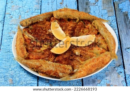Fried small fish on a plate, decorated with lemon slices, blue old board background