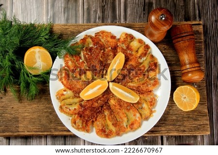Fried small fish on a plate, decorated with lemon slices, brown wooden background