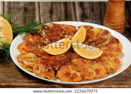 Fried small fish on a plate, decorated with lemon slices, brown wooden background