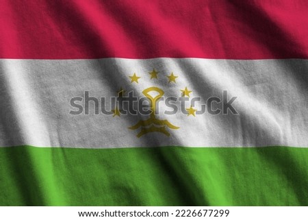 Tajikistan flag with big folds waving close up under the studio light indoors. The official symbols and colors in fabric banner