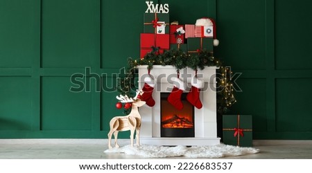 Fireplace with Christmas gifts, socks and wooden deer near green wall in room