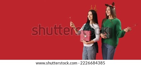 Pretty young women with Christmas sparklers and gifts on red background with space for text
