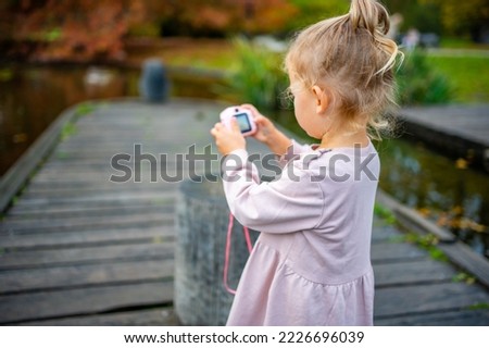 Toddler Girl Taking Pictures with Pink Digital Children's Camera in the Summer Park . High quality photo