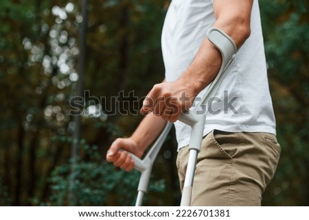 Close up view. Man with crutches is in the park outdoors. Having leg injury. Royalty-Free Stock Photo #2226701381