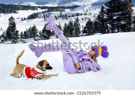 Winter fashion. Beautiful female model is wearing lilac winter outfit, lilac boots and colorful beanie. Attractive young woman in wintertime outdoor. Mountains, white snow in magic winter day.