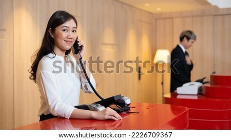Friendly receptionist woman working and call talking to customer by telephone at desk in hotel lobby. Leisure and travel at holidays. beautiful young asian woman receptionists working at a reception