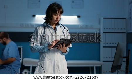 Practitioner doctor holding tablet computer checking patient report while typing medical expertise during night shift in hospital office. Physician woman in white coat working at health care treatment Royalty-Free Stock Photo #2226721689