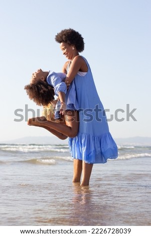Happy family having fun on beach. African American mother and daughter making faces, hugging, laughing, fooling around, jumping. Leisure, family time, fun concept