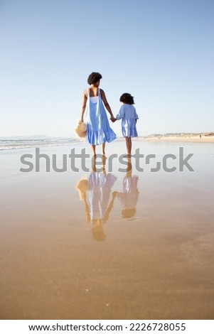 Back view of loving African American family walking on beach. Mother and daughter with dark curly hair spending time together on open air. Leisure, family time, togetherness concept