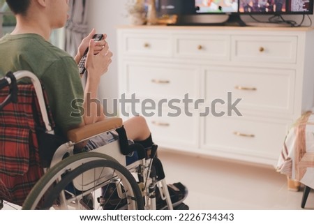 Hands of Young man with a disability using remotcontro for TV in living room at the house for learning,studying or Watch cartoons,Teenage boy use technology, social media,Hobby and education Concept.