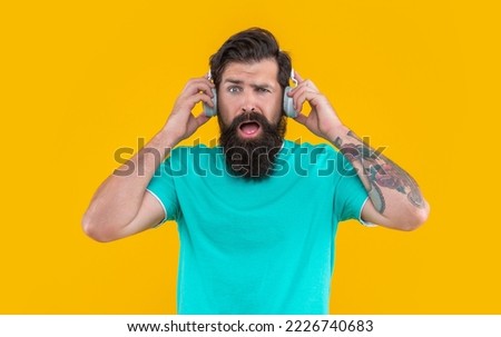 annoyed man has loud music in headphones isolated on yellow. annoyed man listen loud music